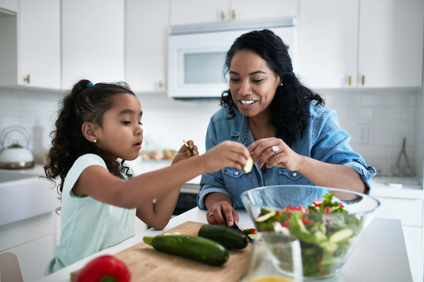 Mother and daughter preparing meal at home. Girl is learning to prepare food from woman. They are in kitchen.