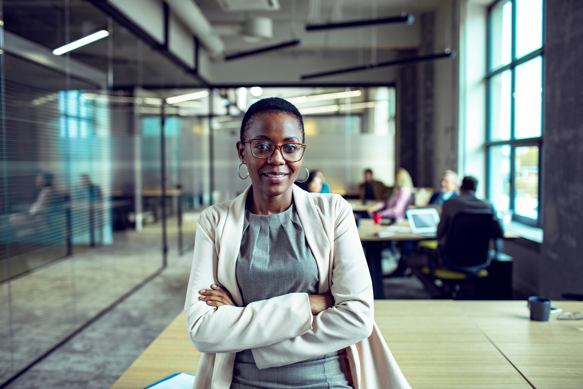 Woman leaning on a table in an office with her arms crossed