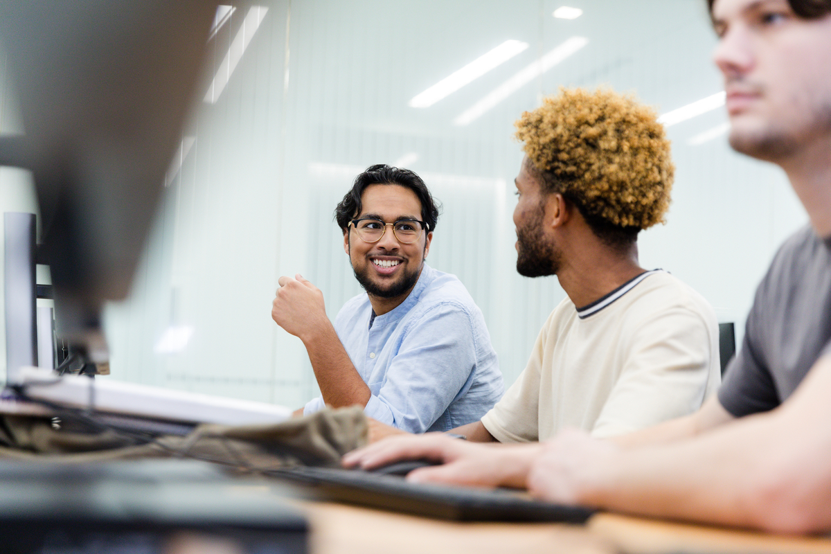 Two diverse young adult male university students get to know each other during computer lab.